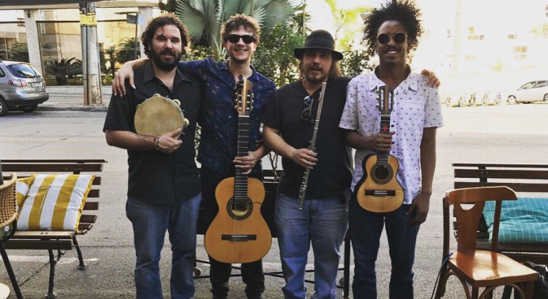 Quatro integrantes de grupo de chorinho posam, de pé, com pandeiro, flauta, violão e cavaquinho. 