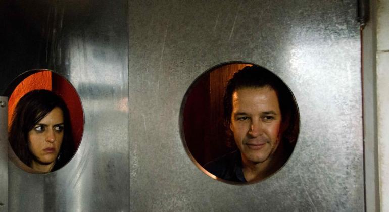 A Fundação Municipal de Cultura exibe, no MIS Cine Santa Tereza, no dia 28/9, às 19h, o premiado filme “O Animal Cordial”. Foto: Divulgação Um homem e uma mulher olham através de círculo de metal da porta; cena do filme "O animal cordial".