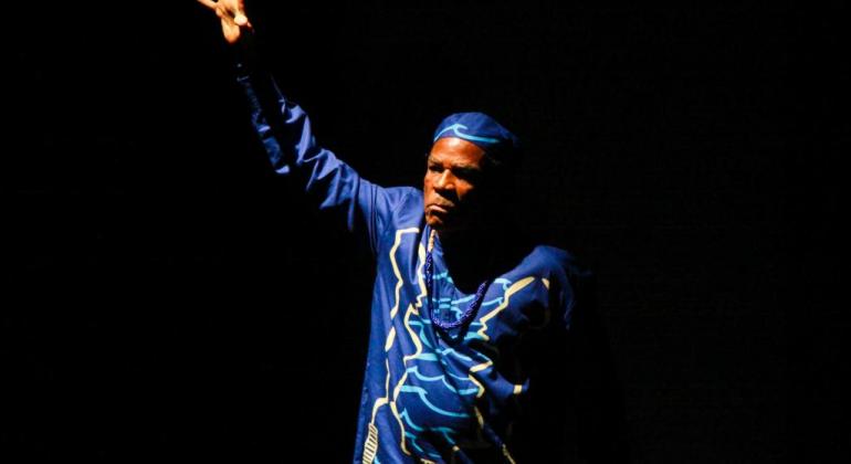 Documentário e peça teatral em torno da família Pitanga fazem parte do Festival de Arte Negra de Belo Horizonte – (FAN-BH). Foto: Fernanda Bezerra O ator Antônio Pitanga, com camiseta e boina azul em fundo escuro, no palco.