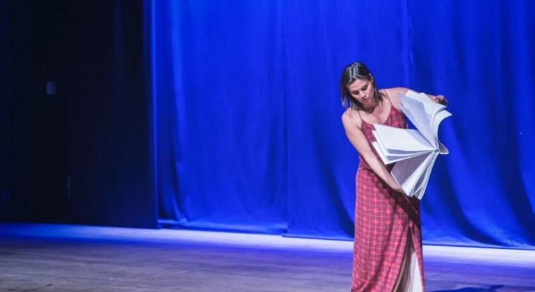 O espetáculo de dança “Sonhos Invisíveis” é destaque no Teatro Raul Belém Machado no dia 30/11, às 20h. Foto: Divulgação PBH Mulher de vestido abe livro com folhas.