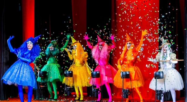 Seis bruxinhas, cada uma de uma cor, se apresentam no palco. 