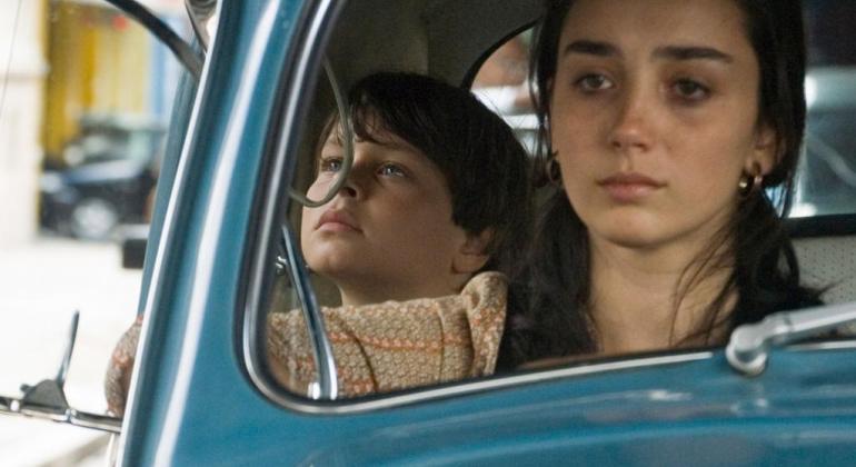 Foto: Divulgação Mulher dirige fusca azul com menino sentado no banco traseiro. Cena do filme "O ano em que meus pais sairam de férias"