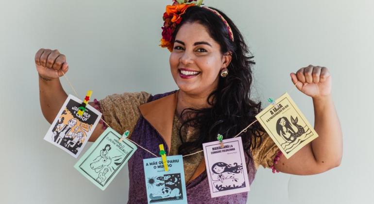 Mostra Infantil do Circuito Municipal de Cultura traz literatura de cordel Mulher segurando barbante com representação da literatura de cordel