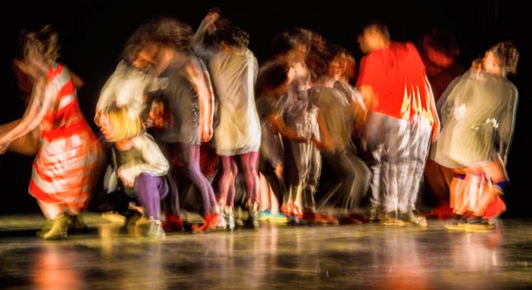 Imagem de pessoas dançando em um palco. Foto feita em modo que demonstra movimento