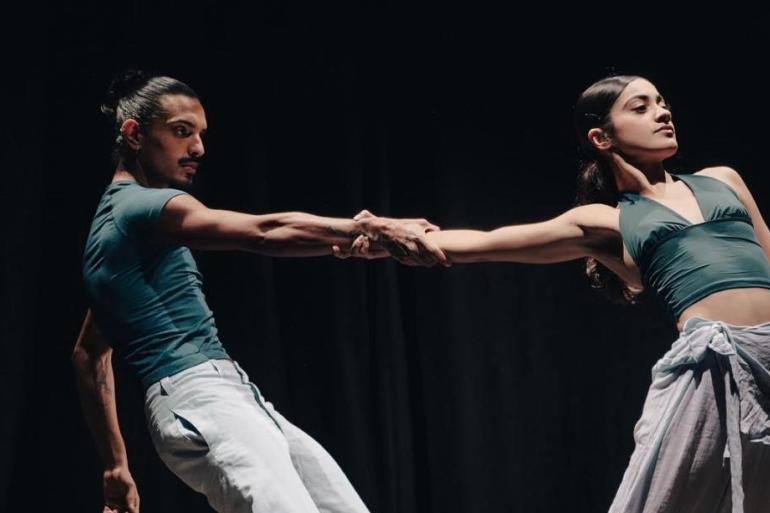 Dança em dose dupla marca a programação do Teatro Francisco Nunes no próximo final de semana A foto mostra dois bailarinos em cena, um homem e uma mulher, vestindo roupas em tons verde-petróleo e calças claras, contra um fundo preto teatral. Eles executam um movimento dramático de dança contemporânea, inclinando seus corpos para lados opostos enquanto mantêm os braços firmemente entrelaçados.