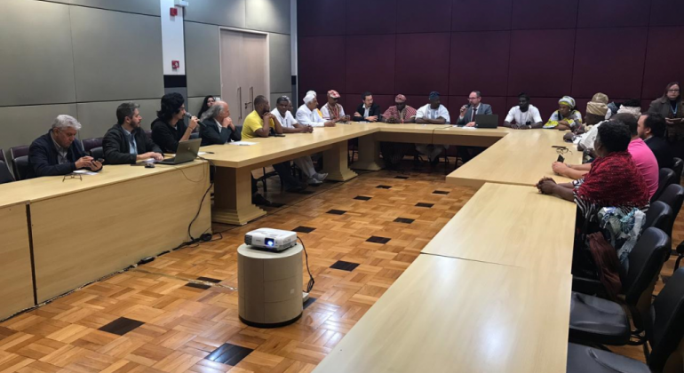 O vice-prefeito de Belo Horizonte, Paulo Lamac, acompanhado de representantes municipais, recebeu uma delegação do estado de Osun, Nigéria. Foto: Divulgação PBH Mesa em forma de "u", com mais de quinze pessoas reunidas.