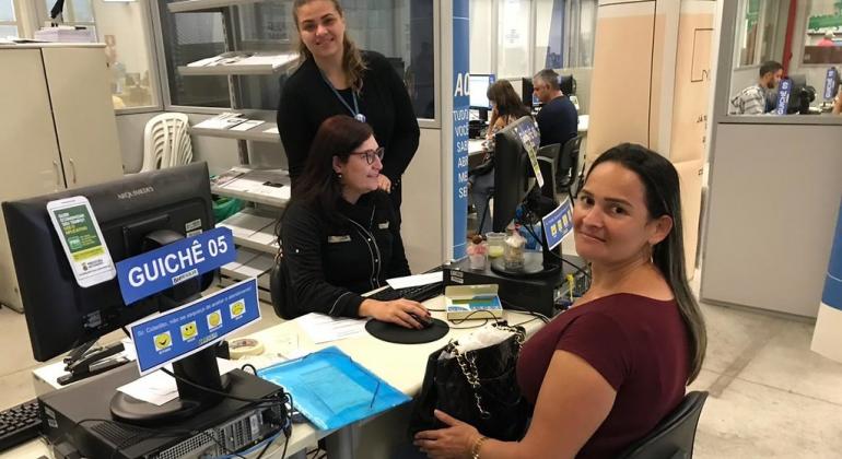 Duas mulheres orientam cidadã em guichê de atendimento. 