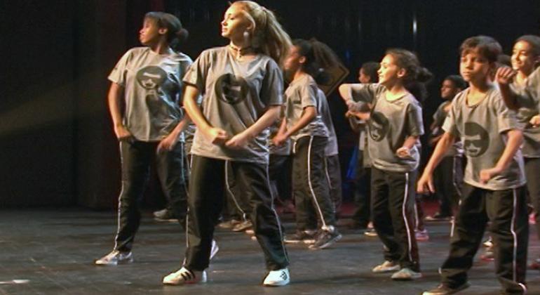 Apresentação artística de alunos do Programa Escola Integrada, com mais de sete alunos no palco. Foto ilustrativa.