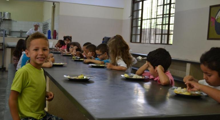 Cerca de quinze crianças merendando na cantina da escola