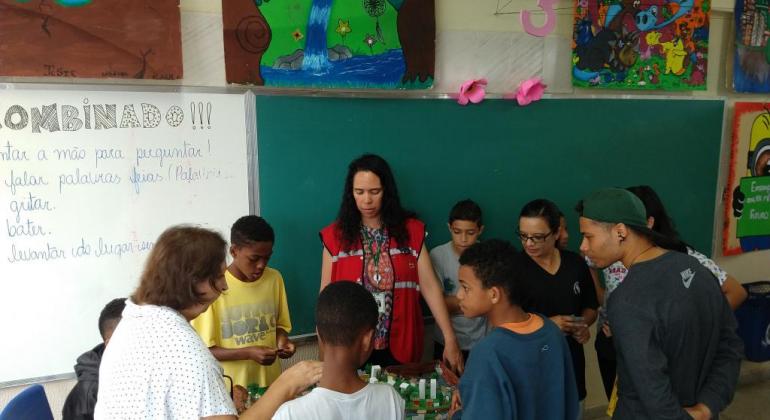 Urbel conscientiza alunos da rede municipal sobre risco geológico e hidrológico. Foto: Divulgação/PBH Alunos e professoras em sala de aula em volta de uma maquete