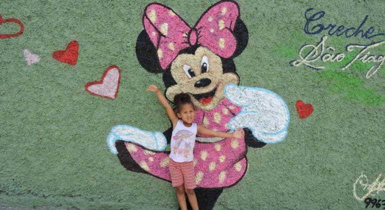 Criança em frente à nova pintura no muro da Creche São Tiago