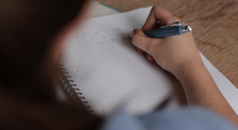 A Prefeitura abre na segunda-feira, dia 2/12, as inscrições para quem quer concorrer a uma bolsa de estudo em escolas particulares. Foto: Divulgação Por cima do ombro de aluno, vemos a mão dele resolvendo uma equação matemática no papel.