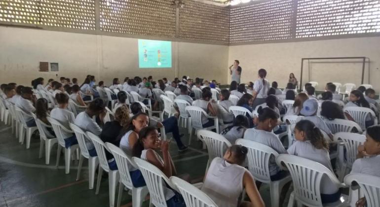 Estudantes da escola Alice Nacif reunidos em pátio da escola, sentados, ouvindo um palestrante