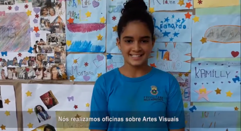 Documentário, animação e ficção são as categorias dos 24 vídeos do VII Festival Educação Integral de Minicurtas. Foto: Divulgação Estudante à frente de uma painel feito por alunos com legenda que diz: "Nós realizamos oficinas sobre Artes Visuais", cena de vídeo documentário Amabilidade da E. M. Santos Dumond.