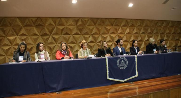 Secretária municipal de Educação, Ângela Dalben, acompanhada de sete pessoas na mesa de abertura da IX Conferência Municipal de Educação. 