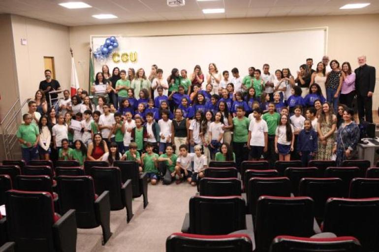 #paratodosverem: Grande grupo de estudantes e educadores se reunem em um auditório para uma foto posada. Crianças e jovens, muitos usando camisetas verdes, azuis e brancas, posam sorridentes ao lado de professores e convidados.