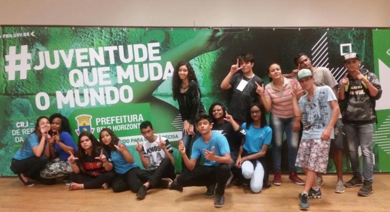 Turma de alunos em frente à banner em que se lê: A juventude que muda o mundo