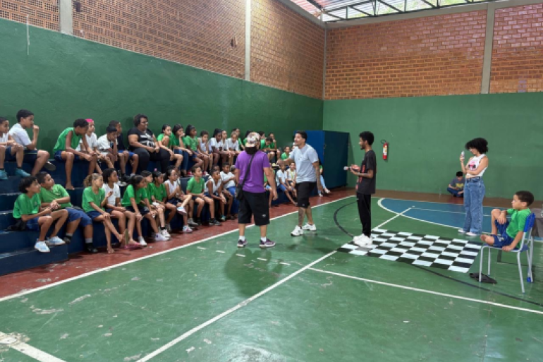 Batalha de rima reúne estudantes em momento de expressão cultural #PARATODOSVEREM: Estudantes do 4º ano participam de uma batalha de rima realizada na quadra da escola, acompanhados por artistas convidados e colegas que observam atentos nas arquibancadas. A atividade integrou música, oralidade e cultura hip-hop em um momento de troca, criatividade e participação coletiva dentro do ambiente escolar.