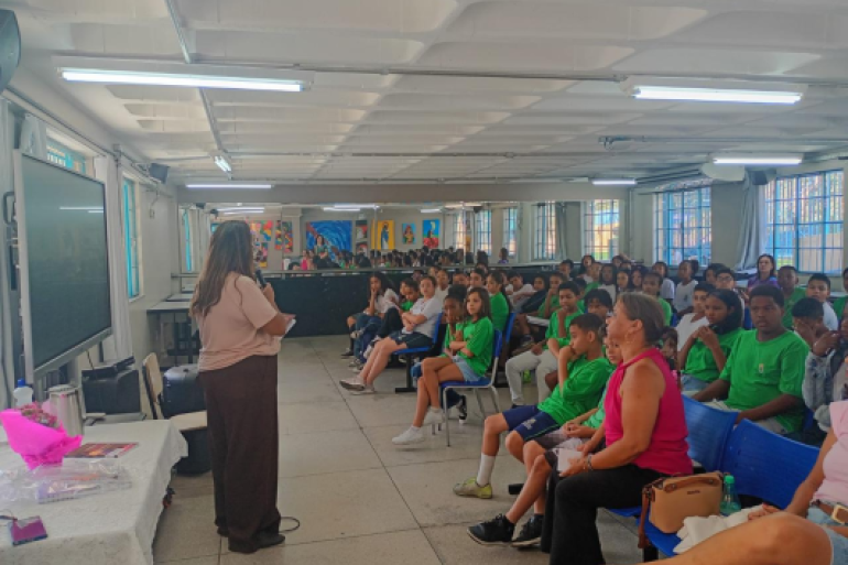 #PARATODOSVEREM: Professora conduz leitura para grupo de crianças sentadas em fileiras, em sala de aula colorida e decorada, acompanhadas por outras educadoras. 