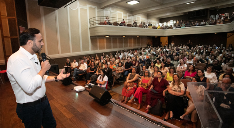 na imagem, o secretário de Educação palestra em um auditório cheio de pessoas.