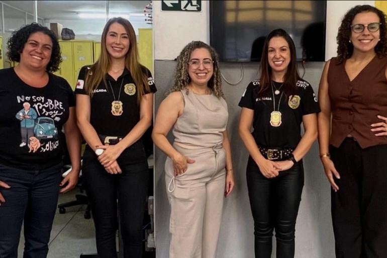 #paratodosverem: Cinco mulheres posam lado a lado, sorrindo para a foto. Duas delas (segunda e quarta mulheres, da esquerda para direita) usam camisetas pretas com identificação da Polícia Civil. 