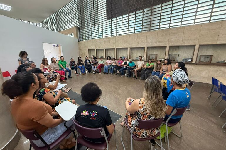 Várias pessoas participam de uma roda de conversa, sentadas em cadeiras dispostas em círculo, em uma sala.