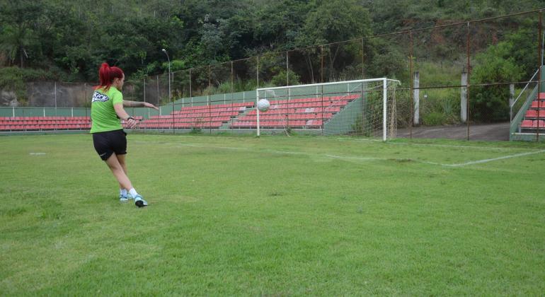 jogadora de futebol feminino chuta bola em direção ao gol no campo.