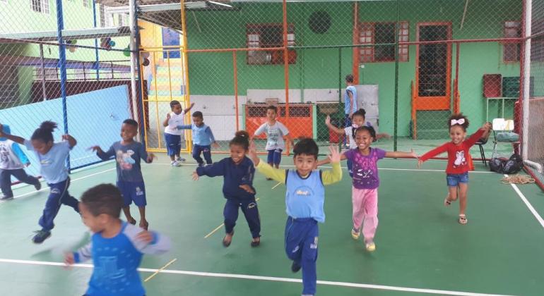 Cerca de dez crianças praticando atividades físicas na quadra da creche