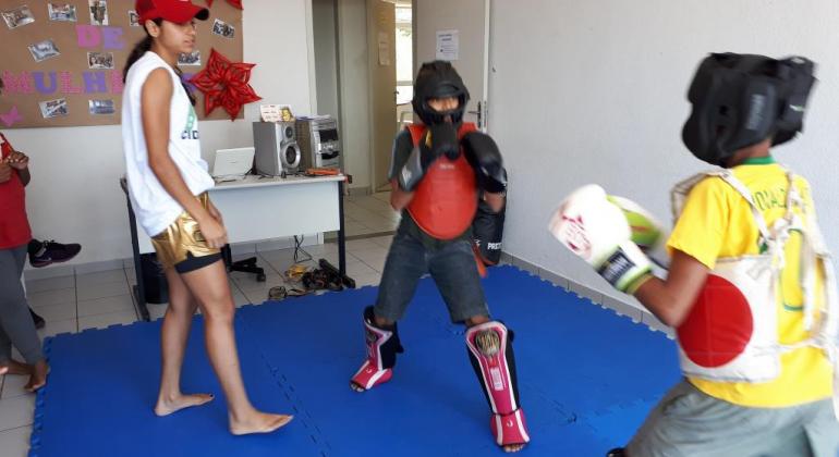 Muay Thai faz parte do calendário de atividades do Programa Esporte Esperança Dois alunos devidamente equipados praticam Muay Thai sob supervisão da professora, em um tatami.