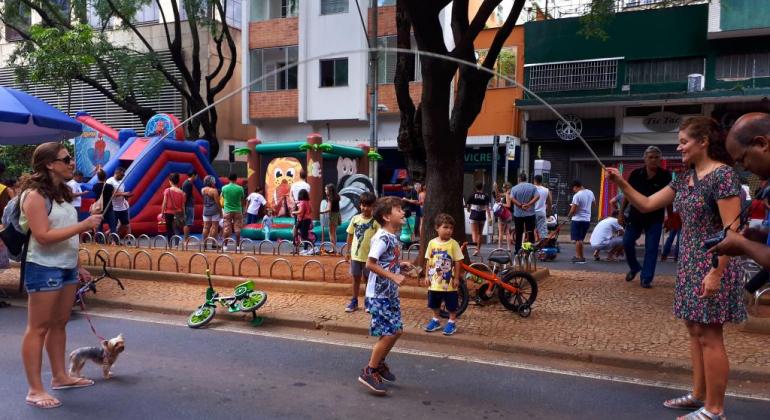 Criança pula corda na Savassi, pessoas transitam ao fundo. 