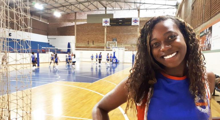 Leila, atleta de vôlei do Olympico pelo programa da Prefeitura. Ao fundo, jovens jogam vôlei no ginásio.