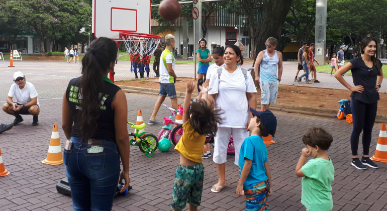 Três crianças jogam basquete, acompanhadas por dois adultos.