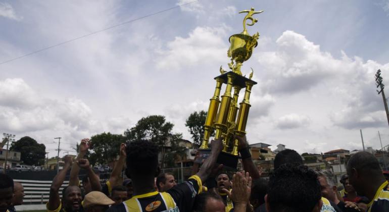 Jogadores do time Castanheira, da categoria Master, comemoram a vitória e erguem a taça, durante o dia. 