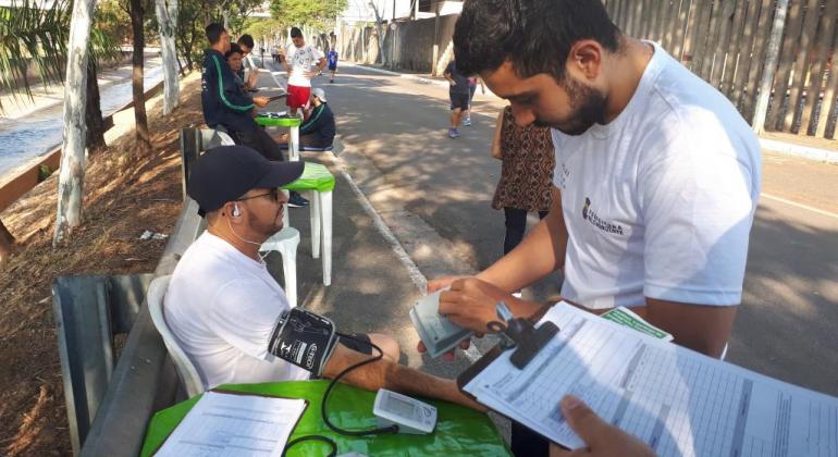 Técnico confere pressão de adepto da caminhada em local aberto, durante o dia. 