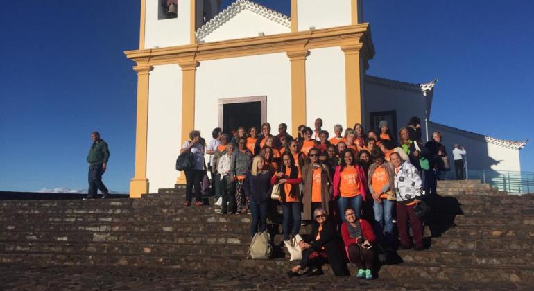 O Instituto Inhotim e o Santuário Basílica da Nossa Senhora da Piedade são os destinos da semana para três grupos do programa da Prefeitura. Foto: Cinthia Santos Cenca de vinte pessoas posam para foto na escadaria, em frente à uma igreja, durante o dia.