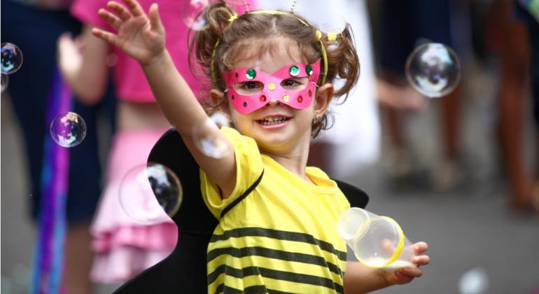 Crianças com máscara de carnaval brinca com bolhas de sabão