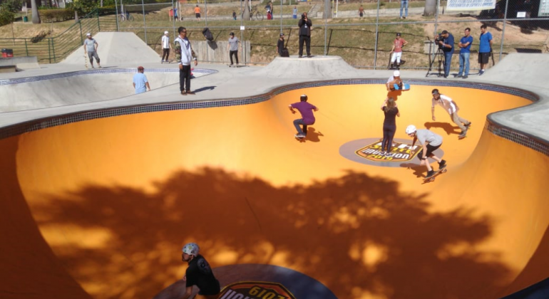 Mais de 130 competidores vão disputar a terceira edição do BH Skate Invasion, realizado nos dias 29 e 30/6 no Parque Fazenda Lagoa do Nado. Foto: Marcelo Machado/PBH Quatro skatistas na pista de skate e nove pessoas observando, durante o dia.