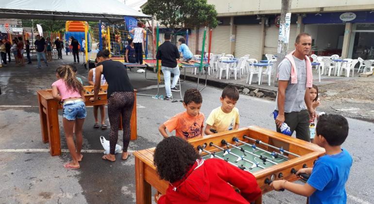 Crianças brincam em volta de uma mesa de pebolim 