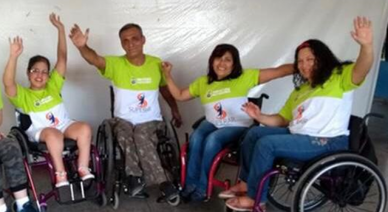 Oficina de percussão e faz ação pela inclusão social de pessoas com deficiência são atrações do BH da Gente de domingo, dia 15/9. Foto: Divulgação PBH Quatro cadeirantes com camisetas do programa Superar, acenam.