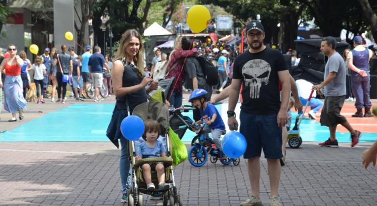 Casal passeia com criança em cadeira de rodinhas e outroas pessoas caminham na Savassi, no domingo, durante o dia. 
