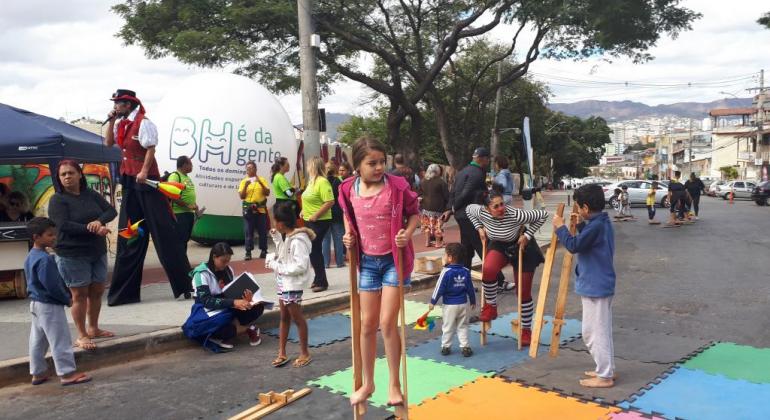 BH é da Gente do dia 20/10 tem blocos de carnaval e ação de orientação nutricional como atrações. Foto: Vilma Tomaz/PBH Crianças brincam de pernas de pau na rua, sobre tapete acolchoado.