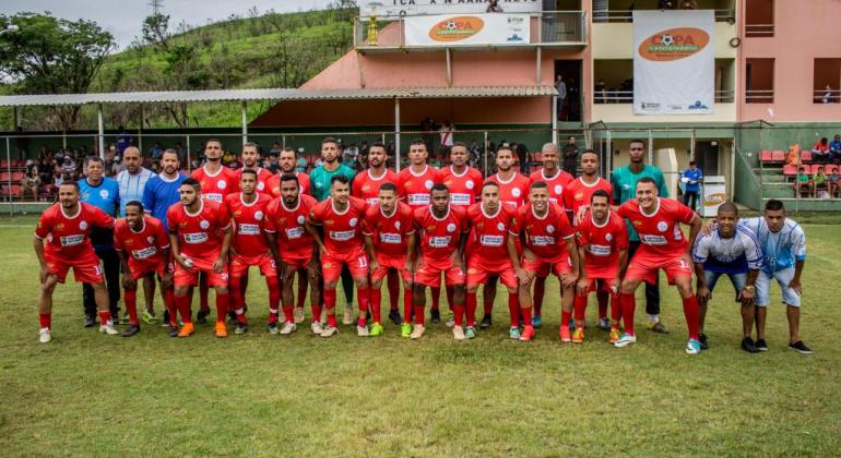 Time de futebol com uniforme vermelho e mais de 20 integrantes posa para foto. 