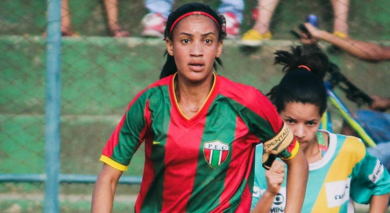 Duas jogadoras de futebol em campo, durante o dia. 