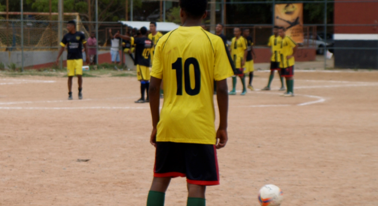 Sete homens jogando futebol, durante o dia. 