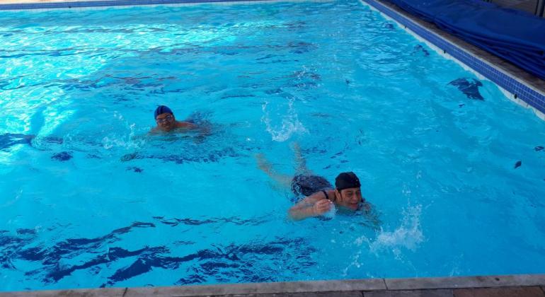 Crianças do programa Superar nadam em piscina, durante o dia. 