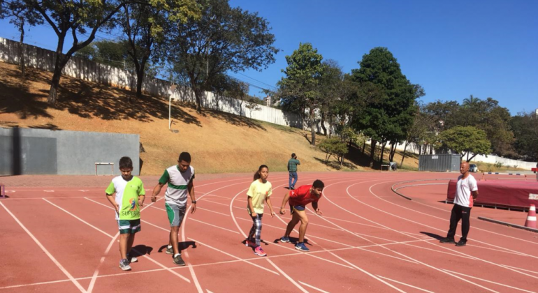 Quatro jovens em pista de corrida, supervisionados por um adulto, durante o dia