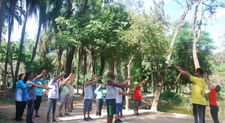 Bem-estar físico, mental e psicológico dos usuários é estimulado por Academia da Cidade. Foto: Mara Damasceno/PBH Cerca de dez pessoas fazem ginástica em contato com a natureza, orientadas por dois técnicos da Prefeitura.