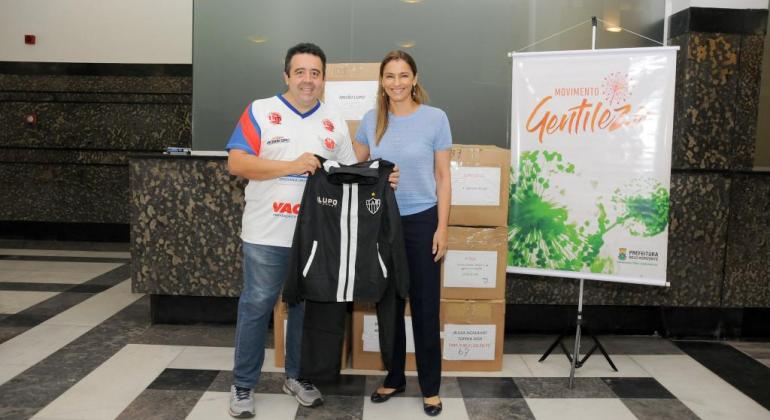 Participantes de programas da Prefeitura e instituições sociais recebem doação de materiais esportivos por meio do Movimento Gentileza. Foto: Divulgação PBH Voluntária social e primeira-dama de Belo Horizonte, Ana Laender, segura roupa esportiva junto a um homem, na Prefeitura.