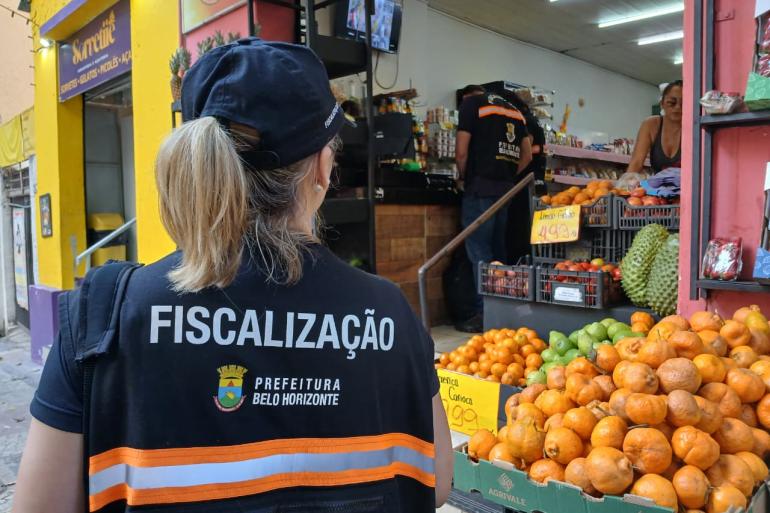 Prefeitura promove ação educativa contra descarte irregular de lixo na Avenida Oiapoque, no Centro de BH Agente de fiscalização da Prefeitura de Belo Horizonte realiza vistoria em estabelecimento comercial. Ao fundo, são exibidos produtos e frutas à venda.