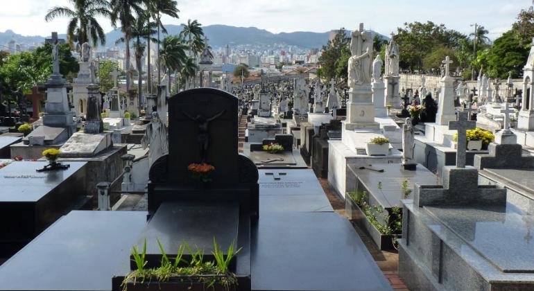 Vários túmulos do Cemitério do Bonfim durante o dia; ao fundo, árvores, a cidade e montanhas. 